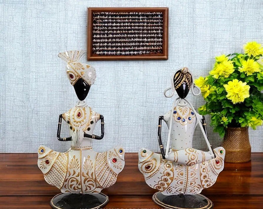 Decorative statues on a wooden surface with a light blue tiled wall and flowers in the background.