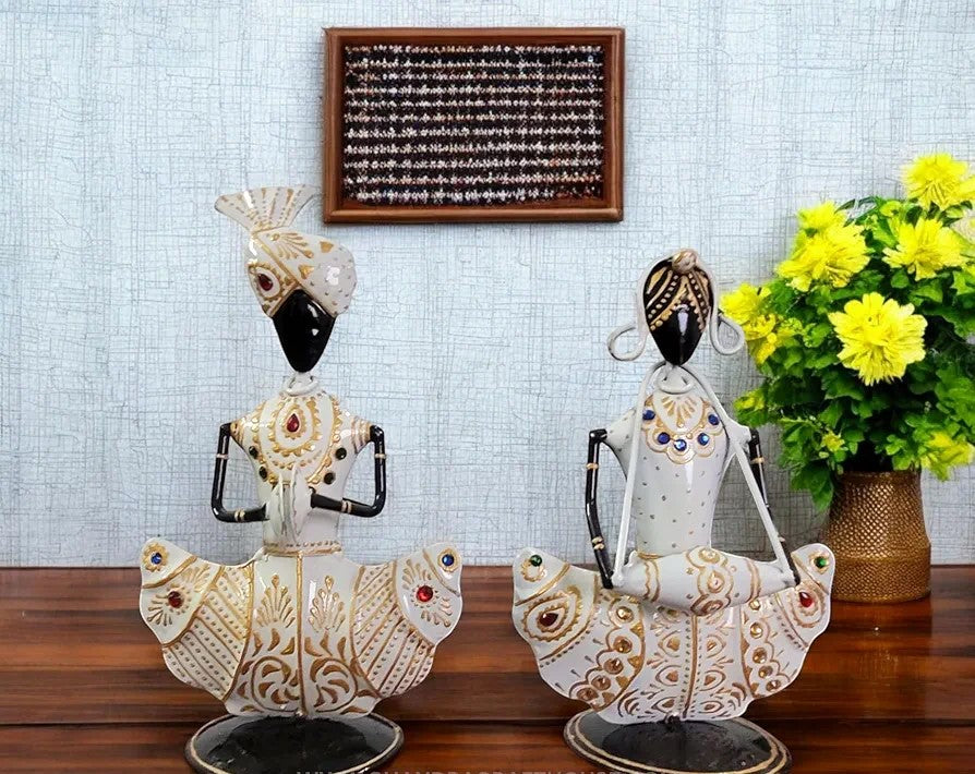 Decorative statues on a wooden surface with a light blue tiled wall and flowers in the background.