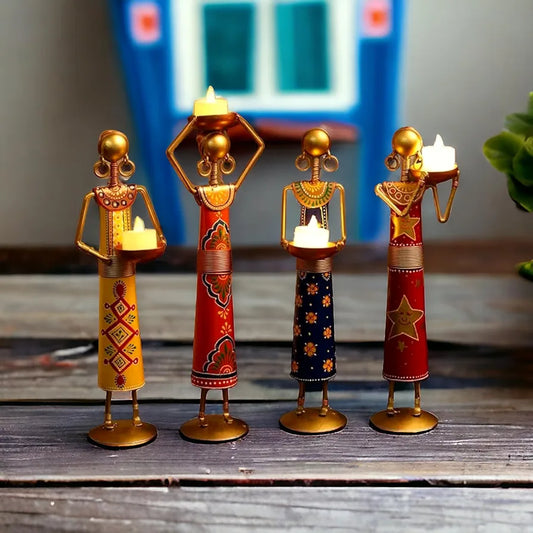 Four decorative candle holders shaped like people on a wooden surface.