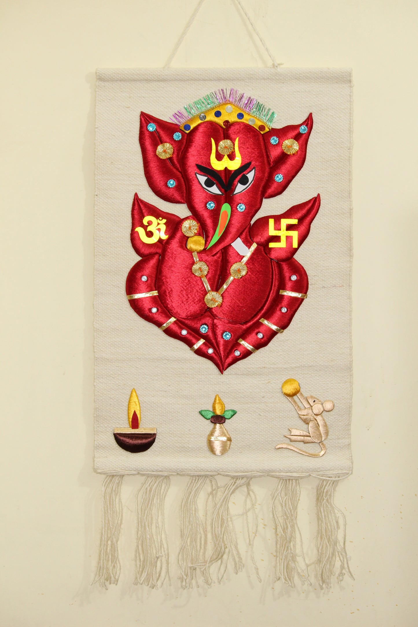 Red and gold silk embroidered Ganesh Ji spiritual wall art mat on a rustic beige jute backdrop
