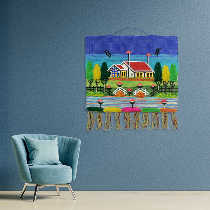 Decorative handwoven jute village scenery tapestry with a blue sky background styled as wall art in a modern living room