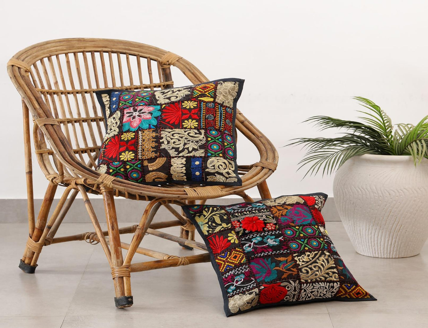 Decorative pillows with colorful patterns on a wicker chair, with a plant in the background.