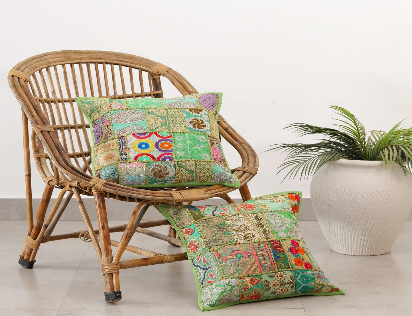 Handcrafted colorful patchwork cushion covers on a vintage wicker chair next to a white potted plant.