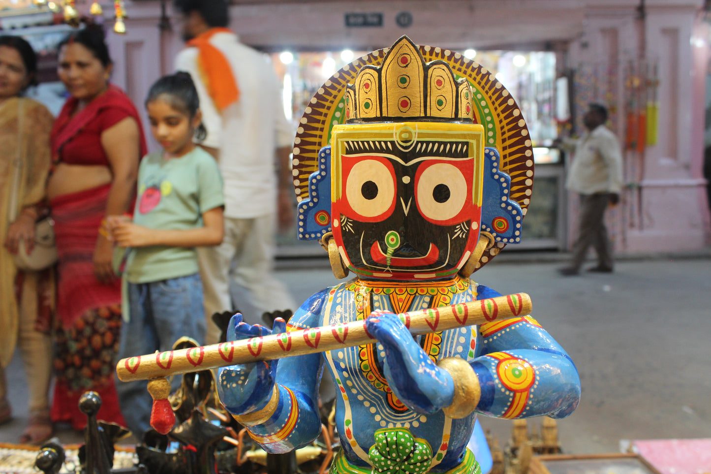Intricate hand-painted facial features showcasing the distinct eyes of Lord Jagannath on a wooden flute-playing Krishna statue.