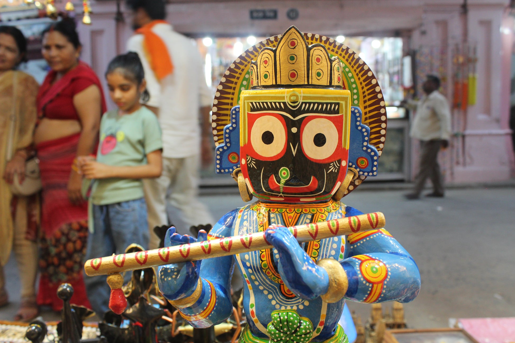 Intricate hand-painted facial features showcasing the distinct eyes of Lord Jagannath on a wooden flute-playing Krishna statue.