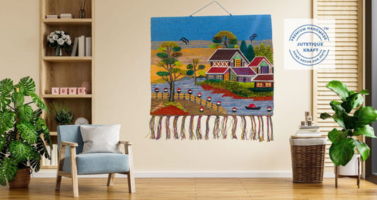 Decorative tapestry of a village scene hanging on a wall in a room with furniture and plants.
