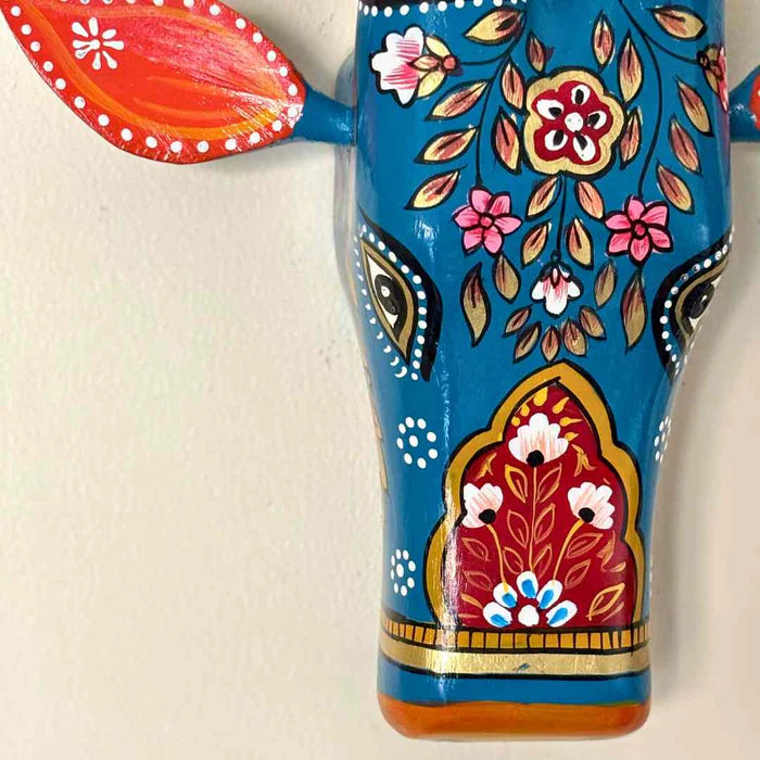 Hand-painted blue wooden cow head wall decor featuring traditional Indian floral patterns and colorful horns.