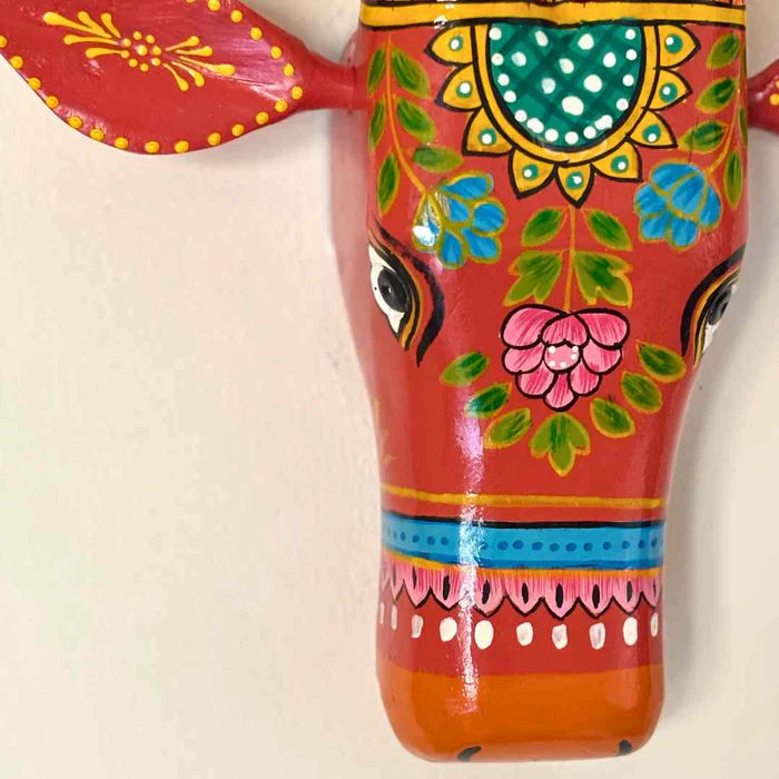 Hand-painted red wooden cow head wall decor featuring traditional Indian floral patterns and colorful horns.