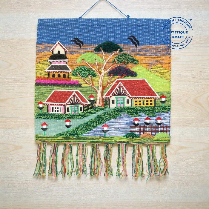 Earthy natural fiber spiritual wall hanging depicting a sacred countryside temple beneath a vibrant blue sky