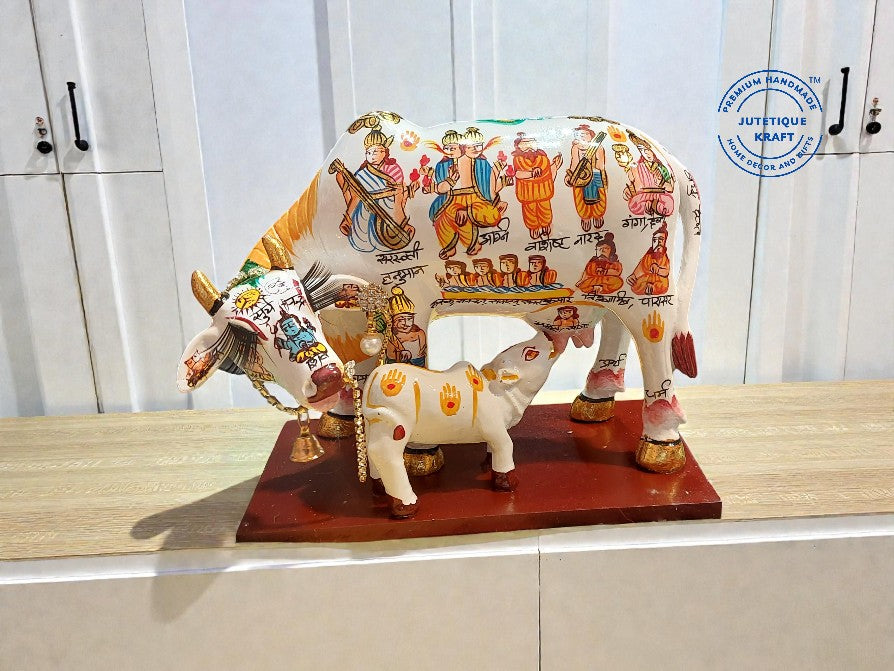 Decorative cow statue with colorful designs on a wooden base against a white background