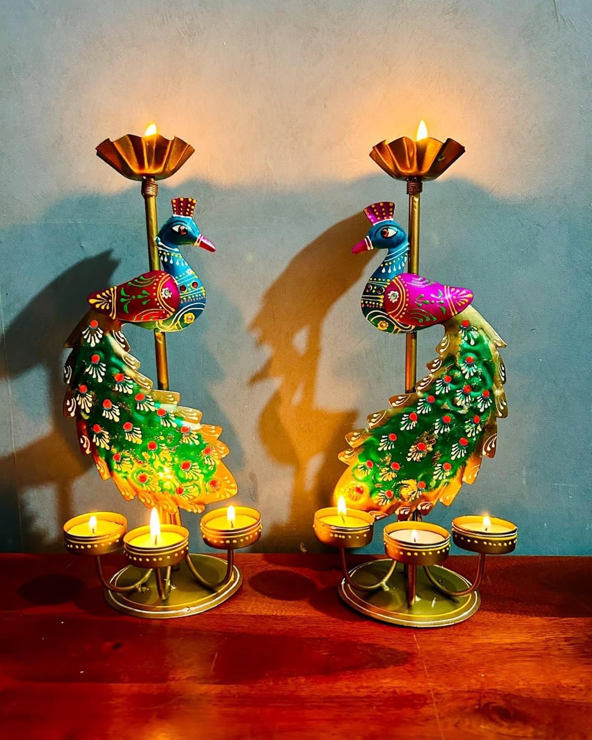 Decorative peacock-shaped candle holders with lit candles on a wooden surface and light blue background.