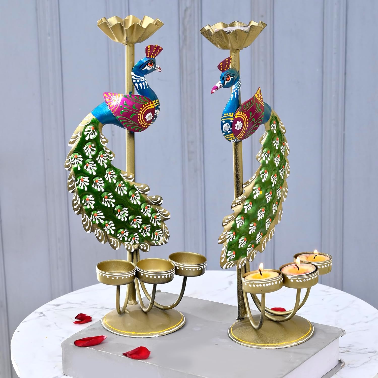 Decorative peacock candle holders with candles on a marble surface.