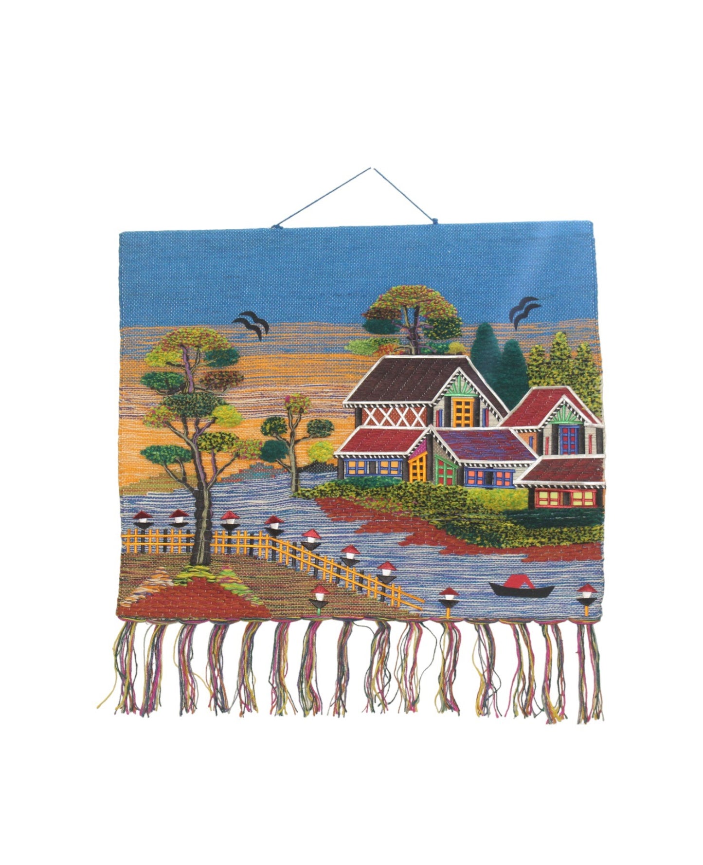Decorative handwoven jute tapestry of a peaceful village scene hanging on a wall in a furnished room with plants