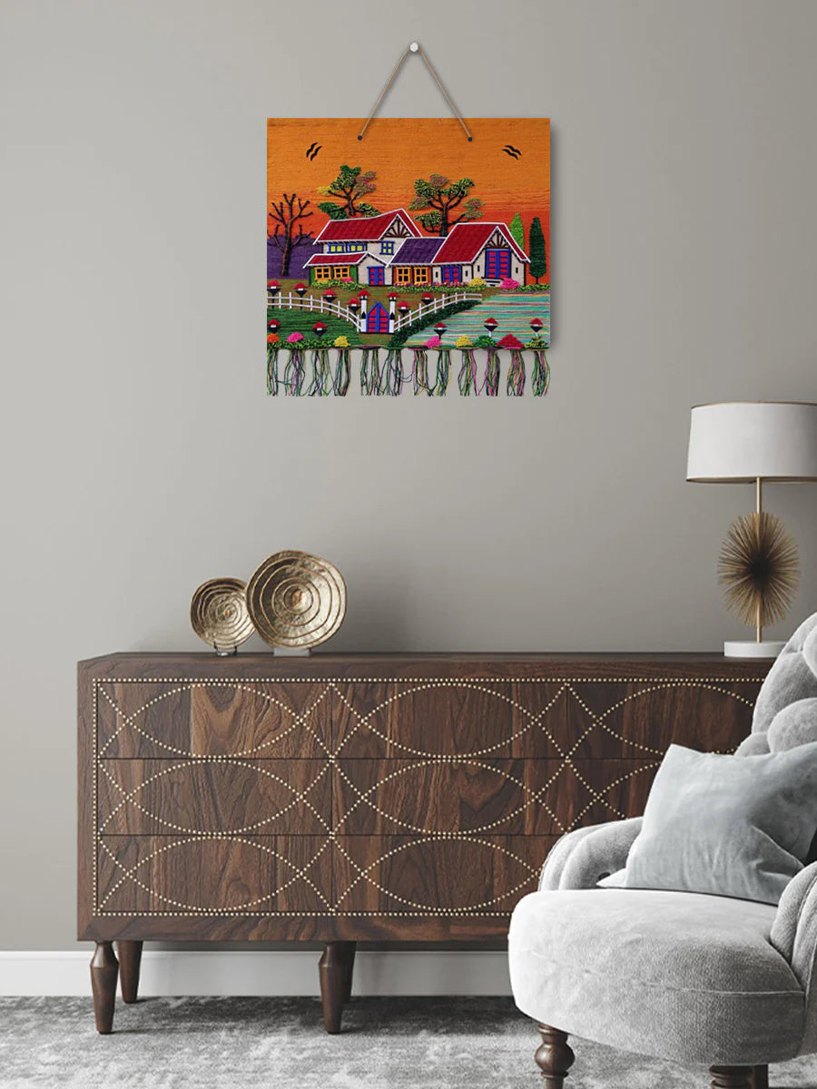 Large traditional handwoven jute village scenery tapestry hanging as a statement art piece above a wooden cabinet in a stylized living room