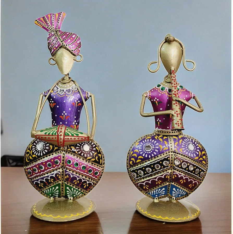 Two ornate purple metal folk musician figurines are displayed on a rustic wooden table against a light blue background