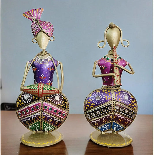 Two ornate purple metal folk musician figurines are displayed on a rustic wooden table against a light blue background