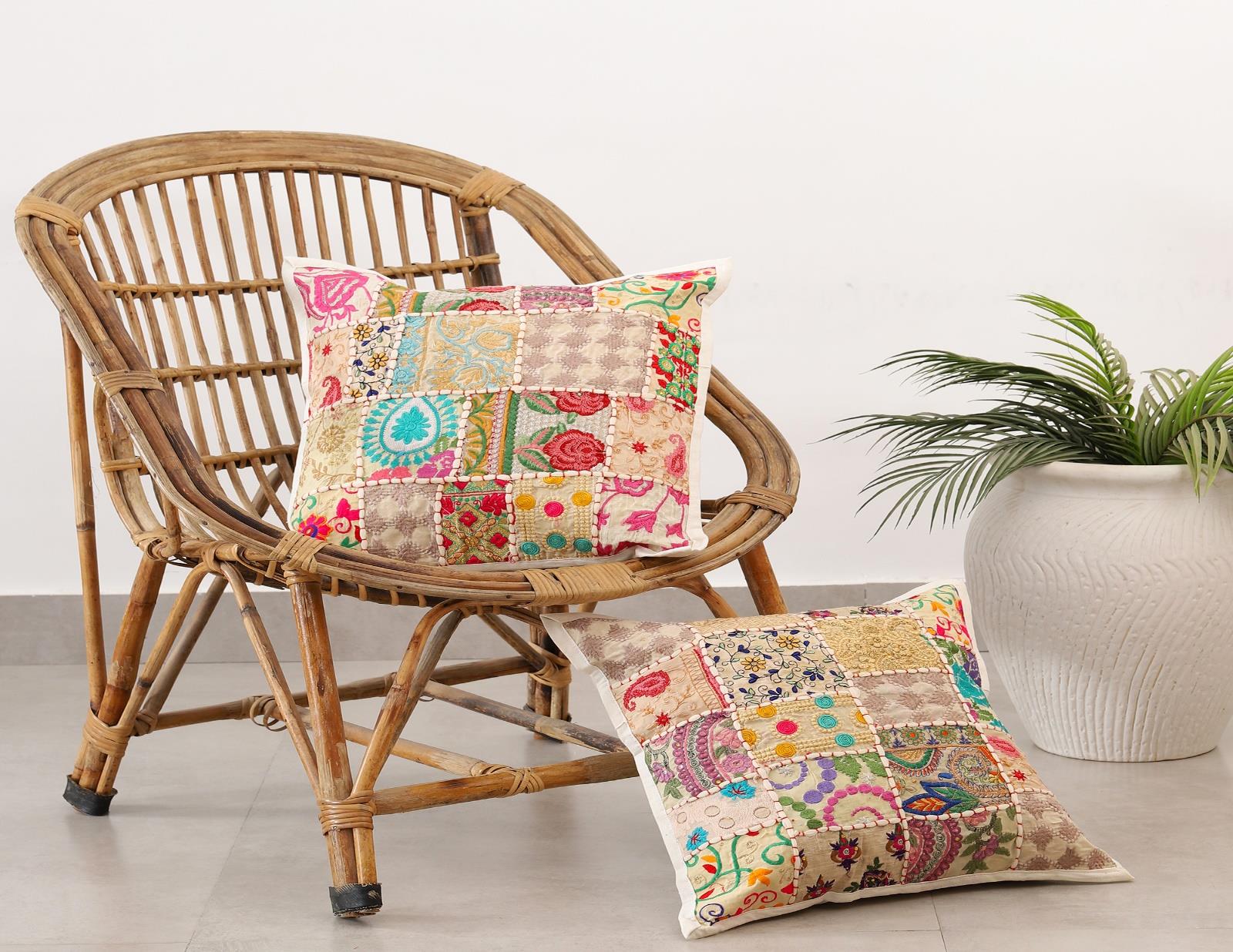 Handcrafted colorful patchwork cushion covers on a vintage wicker chair next to a white potted plant.