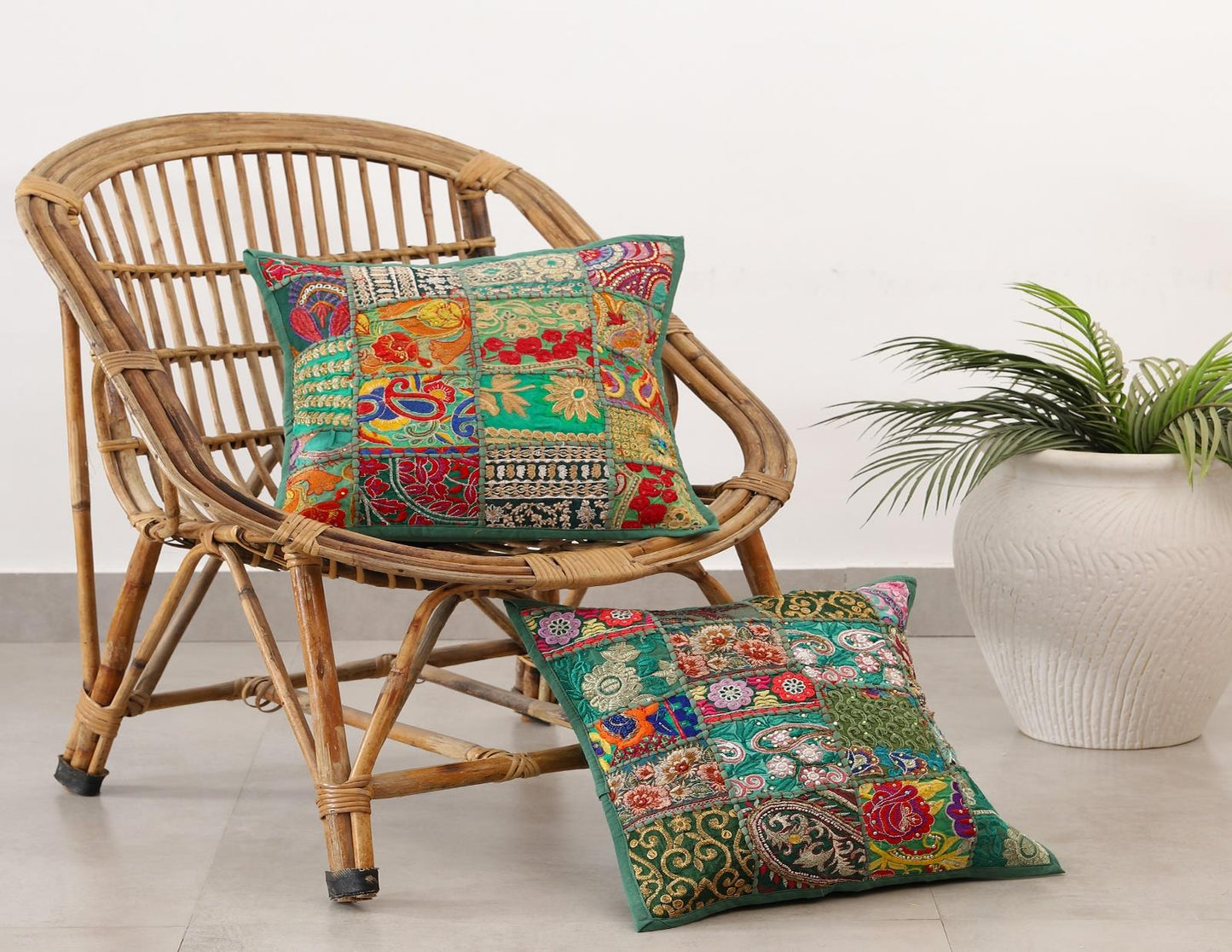 Decorative pillows with floral patterns on a wicker chair and floor, with a plant in the background.