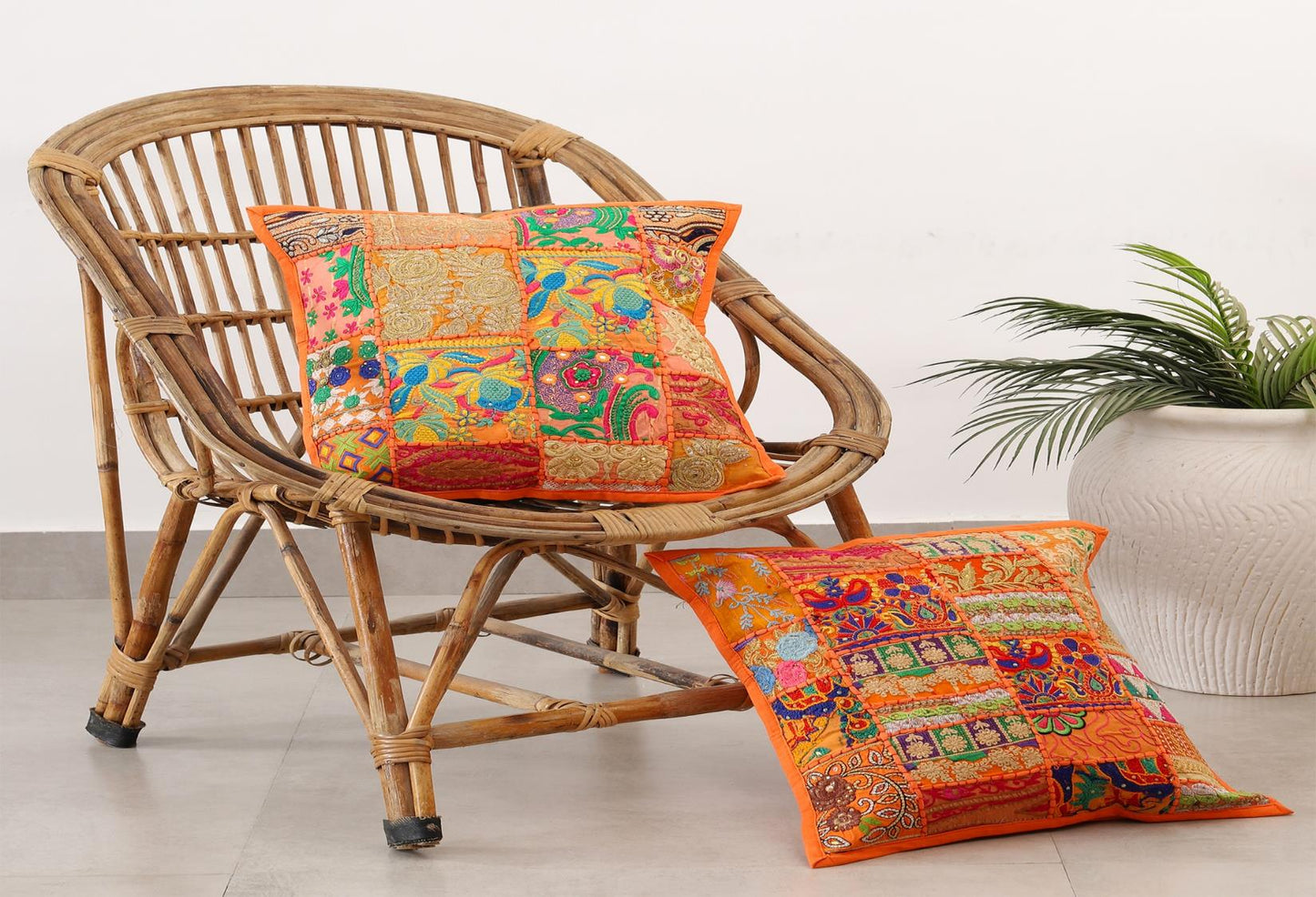 Handcrafted colorful patchwork cushion covers on a vintage wicker chair next to a white potted plant.