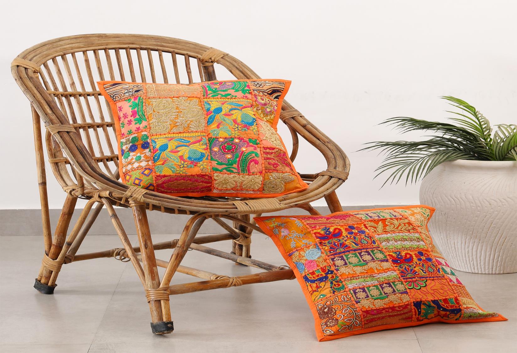 Handcrafted colorful patchwork cushion covers on a vintage wicker chair next to a white potted plant.