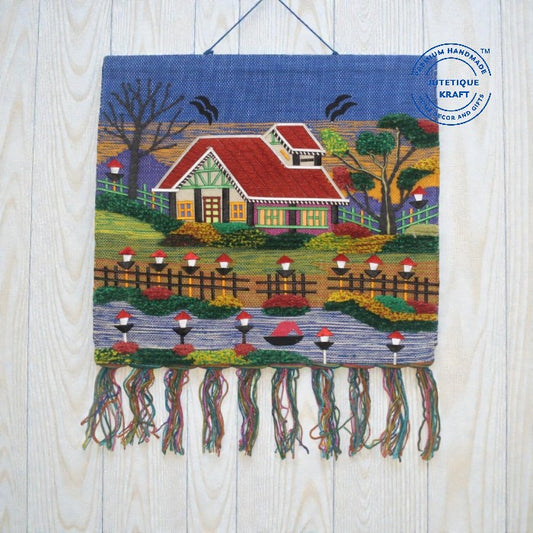 Hand-embroidered cottage tapestry wall hanging named The Red Cabin Scenery, featuring a red-roofed house surrounded by green trees, birds, and decorative border fringes by Jutetique Kraft.